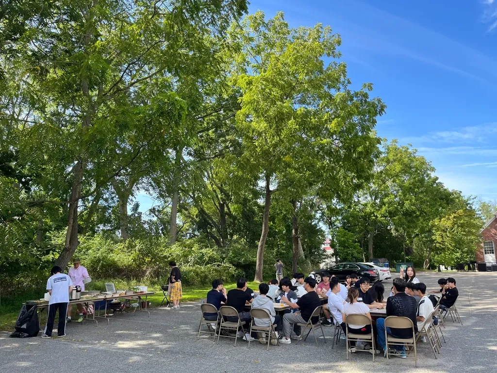 Students from Stony Brook Church sharing a meal outdoors under leafy trees